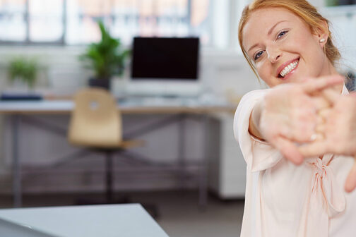 Frau im Büro am Tisch dehnt ihre Hände und Arme.