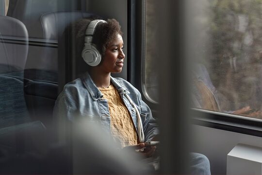 Junge Frau sitzt mit Kopfhörern in einem Bahnabteil und lächelt.