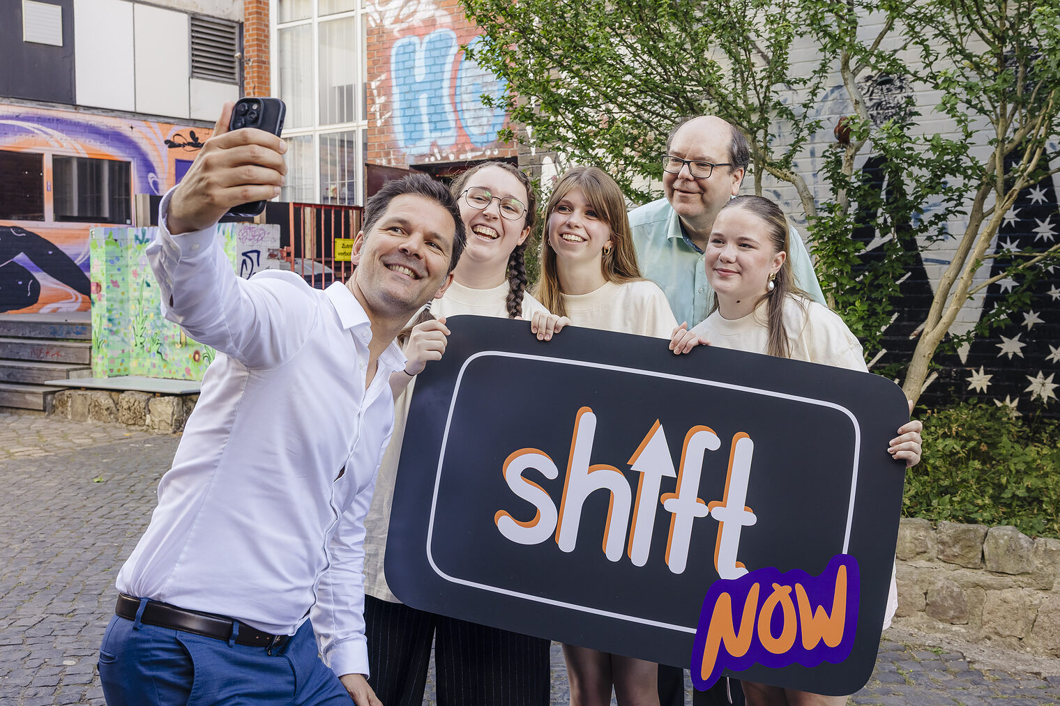Regionspräsident Steffen Krach und Niedersachsens Umweltminister Christian Meyer machen gemeinsam mit Jugendlichen ein Selfie vor einem Plakat mit der Aufschrift ShiftNow.