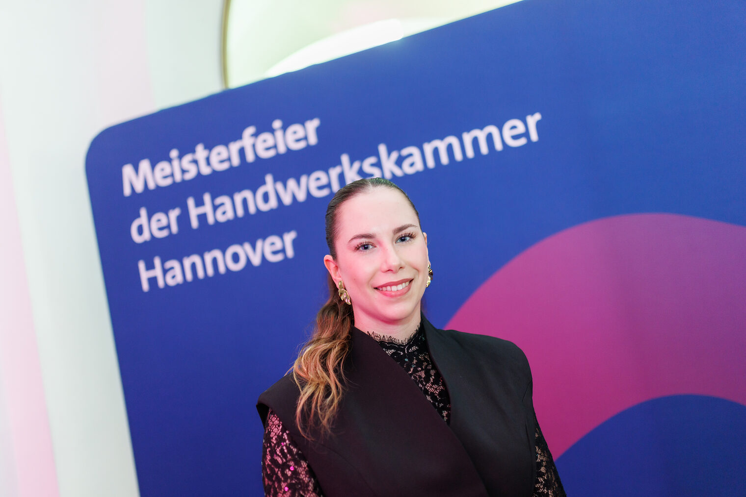 Porträt von Lara Rothemann vor einer Leinwand mit der Aufschrift Meisterfeier der Handwerkskammer Hannover.