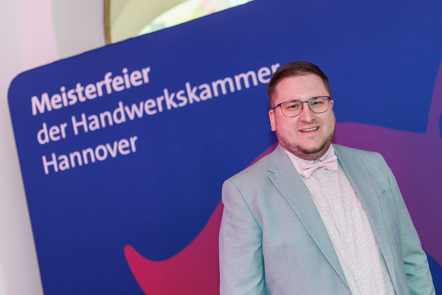 Porträt von Elektrotechnikermeister Sönke Pingel vor Leinwand mit der Aufschrift Meisterfeier der Handwerkskammer Hannover.