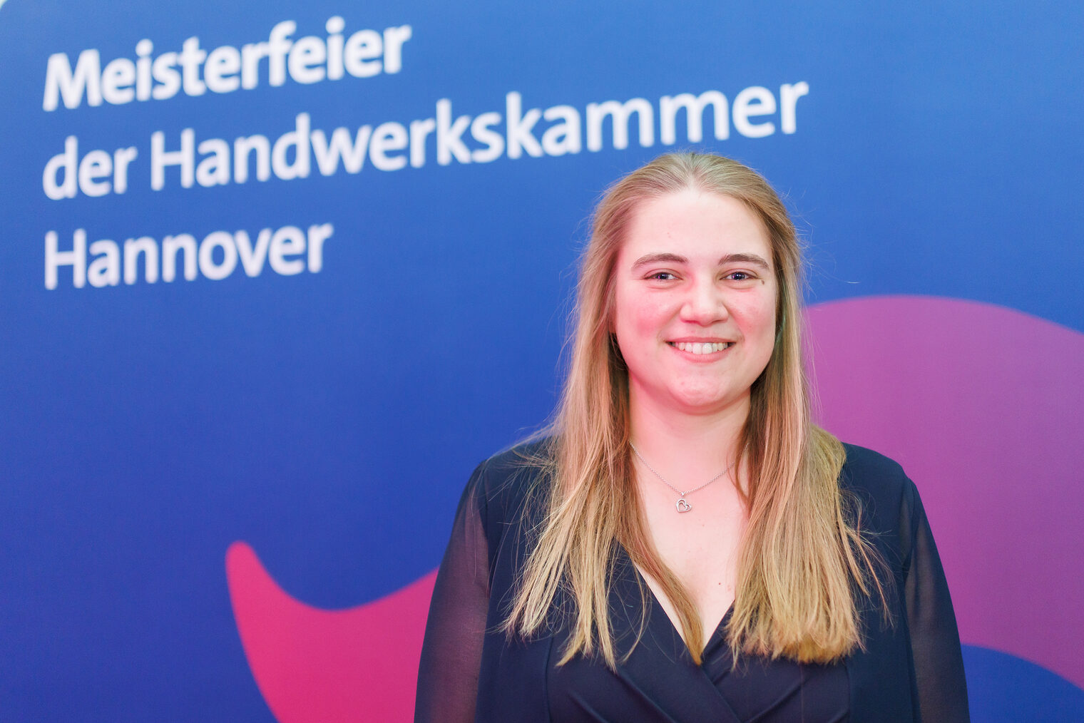 Porträt von Schornsteinfegermeisterin Rieke Bößling vor Leinwand mit der Aufschrift Meisterfeier der Handwerkskammer Hannover.