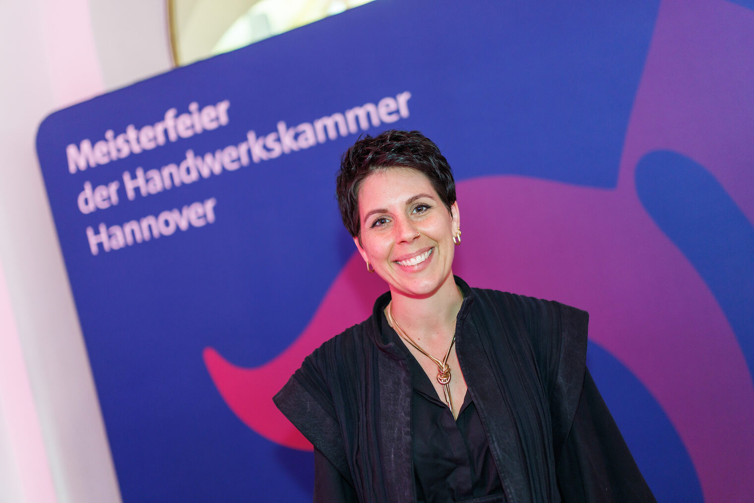 Porträt von Maßschneidermeisterin Anika Baum vor Leinwand mit der Aufschrift Meisterfeier der Handwerkskammer Hannover.