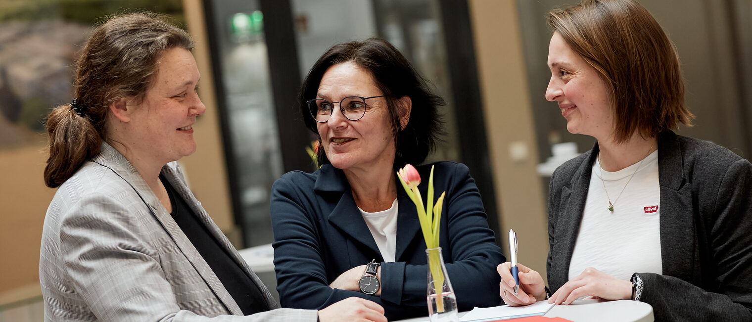 Drei Frauen an einem Stehtisch, die sich unterhalten.