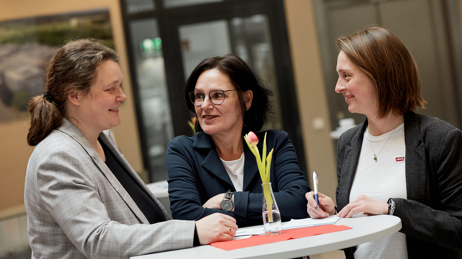 Drei Frauen an einem Stehtisch, die sich unterhalten.