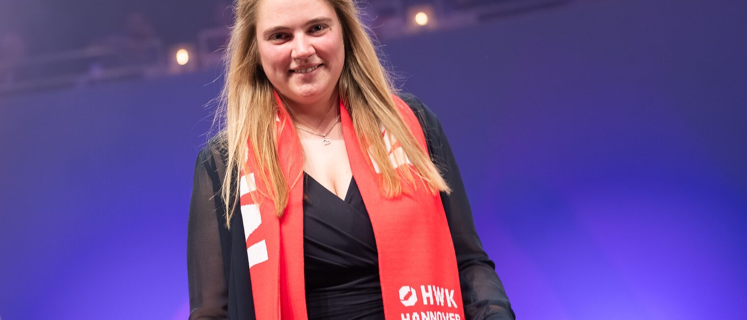 Porträt von Schornsteinfegermeisterin Rieke Bößling bei der Meisterfeier 2025 mit Meister-Schal und Geschenk im Scheinwerferlicht.