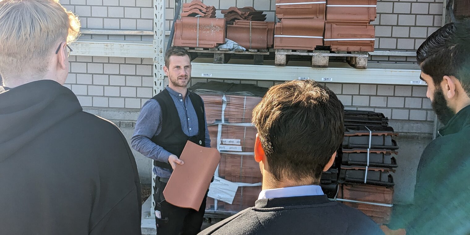 Dachdeckermeister Florian Kastner zeigt einen Ziegel, Jugendliche schauen zu.