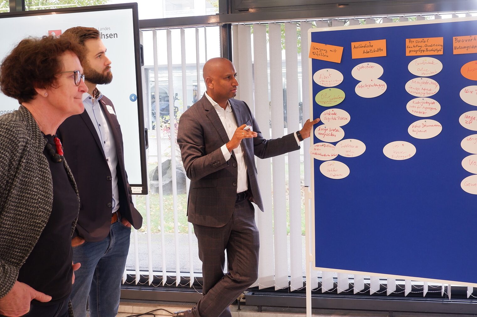 Drei Personen stehen am Flipchart und pinnen Moderationskarten an.
