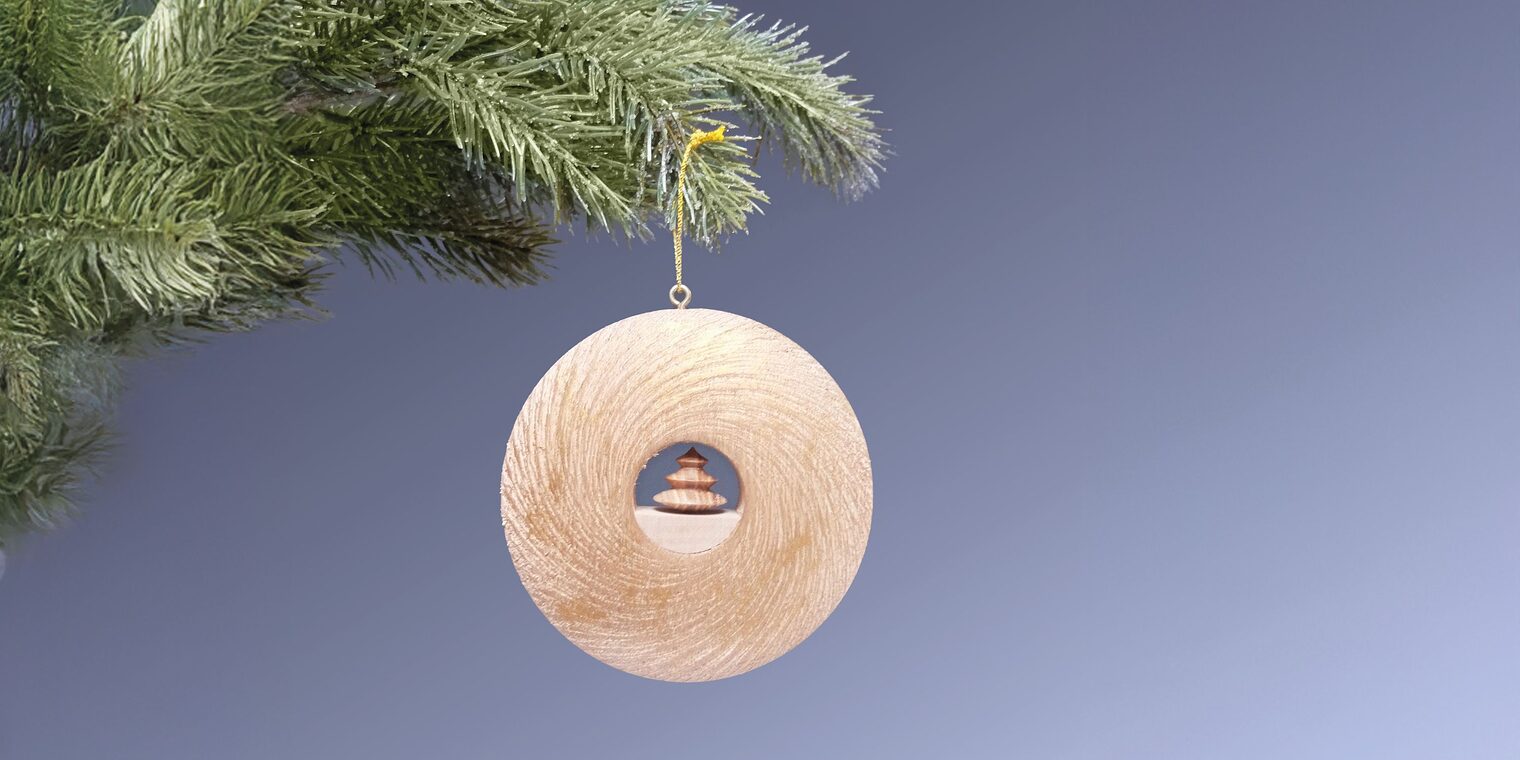 Runder Holzanhänger-Ring mit kleinem Weihnachtsbaum in der Mitte hängt an Tannenzweig.