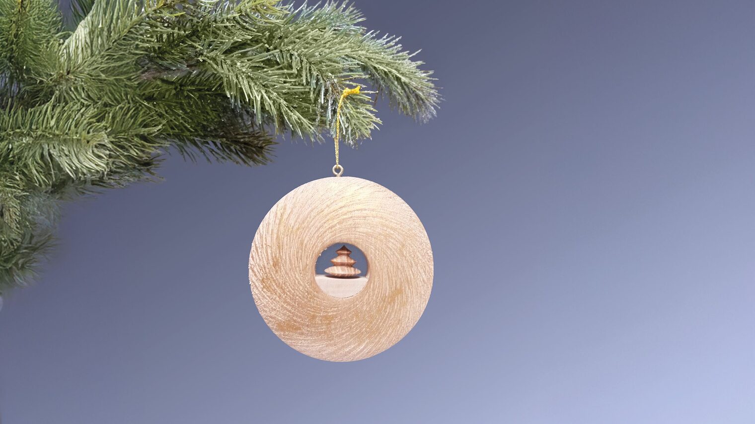 Runder Holzanhänger-Ring mit kleinem Weihnachtsbaum in der Mitte hängt an Tannenzweig.