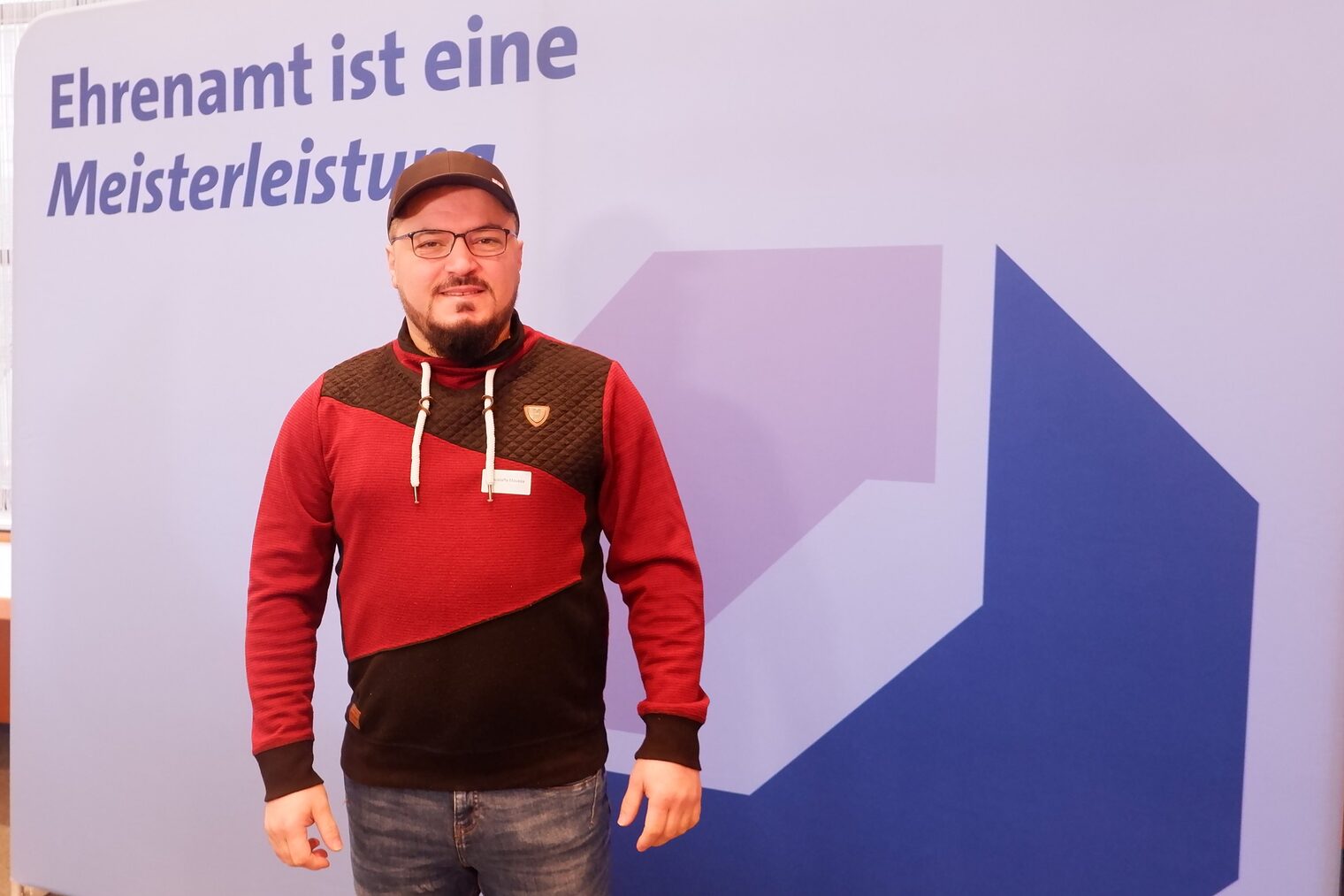Mustafa Moussa vor einer Leinwand mit der Aufschrift: Ehrenamt ist Meisterleistung.