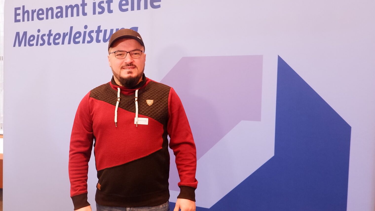 Mustafa Moussa vor einer Leinwand mit der Aufschrift: Ehrenamt ist Meisterleistung.
