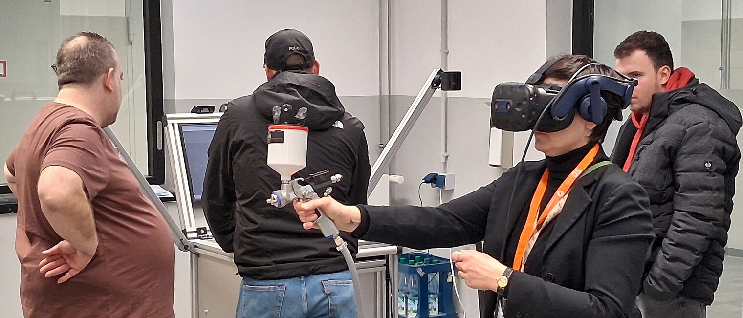 Melanie Staffa-Kuhnt probiert mit der Lackierpistole und einer Virtual Reality-Brille den virtuellen Lacksimulator aus.