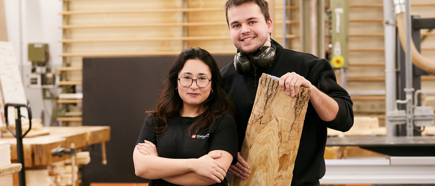 junge Frau und junger Mann nebeneinander in einer Tischlerwerkstatt.