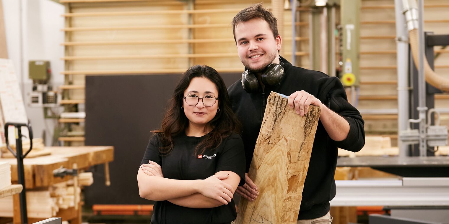 junge Frau und junger Mann nebeneinander in einer Tischlerwerkstatt.