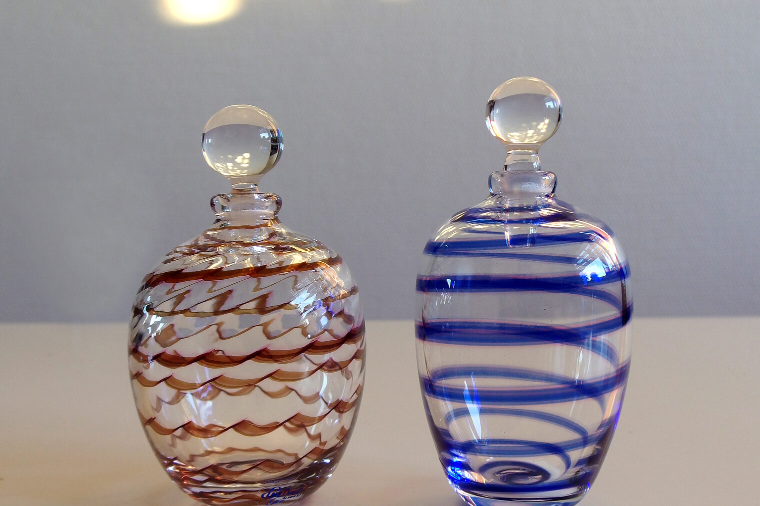 Zwei Parfümfläschchen aus Glas, eine mit roten Linien, eine mit blauen.