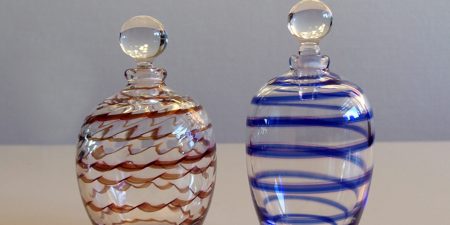 Zwei Parfümfläschchen aus Glas, eine mit roten Linien, eine mit blauen.