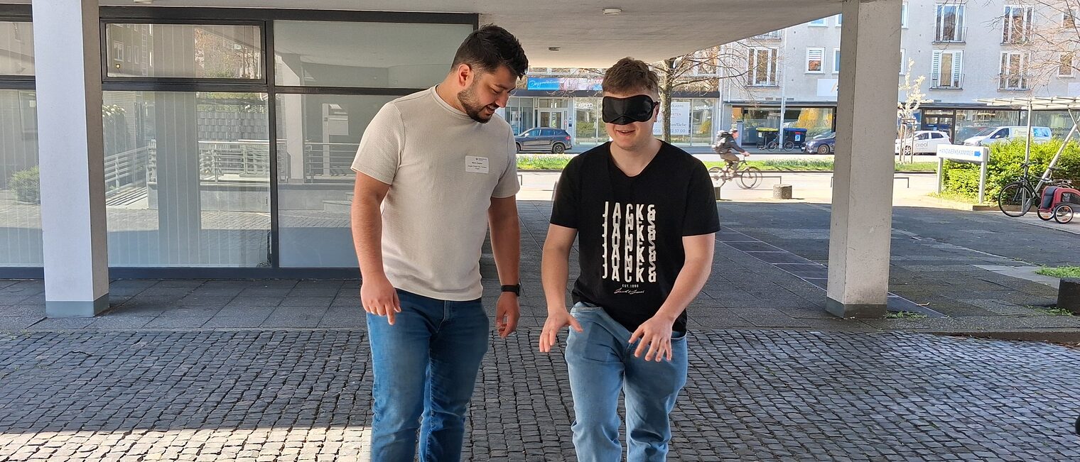 Ein Geselle lotst einen anderen mit verbundenen Augen drei Treppenstufen hoch.