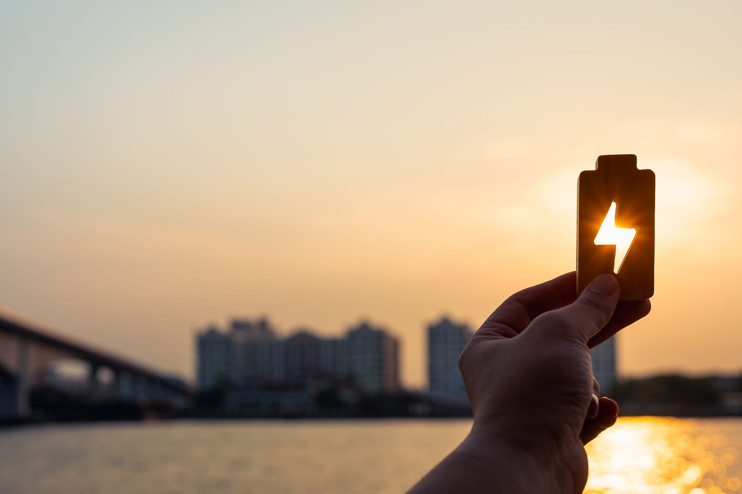Stadtpanorama, Sonne, Hand hält Batterie mit Energiesymbol gegen Sonne