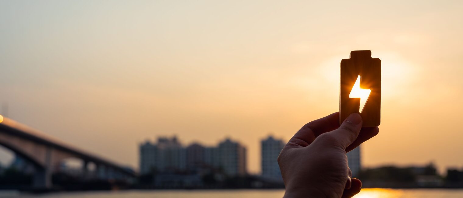 Stadtpanorama, Sonne, Hand hält Batterie mit Energiesymbol gegen Sonne
