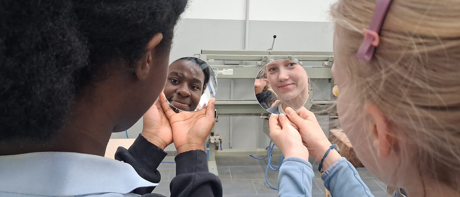 Zwei Mädchen gucken sich in ihren selbst ausgeschnittenen Schminkspiegel an.