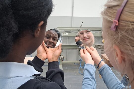 Zwei Mädchen gucken sich in ihren selbst ausgeschnittenen Schminkspiegel an.