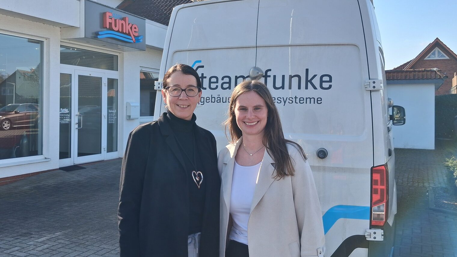 Marion Sievert und Hannah Diephaus stehen draußen vor einem Firmenwagen auf dem Hof von Team Funke. 