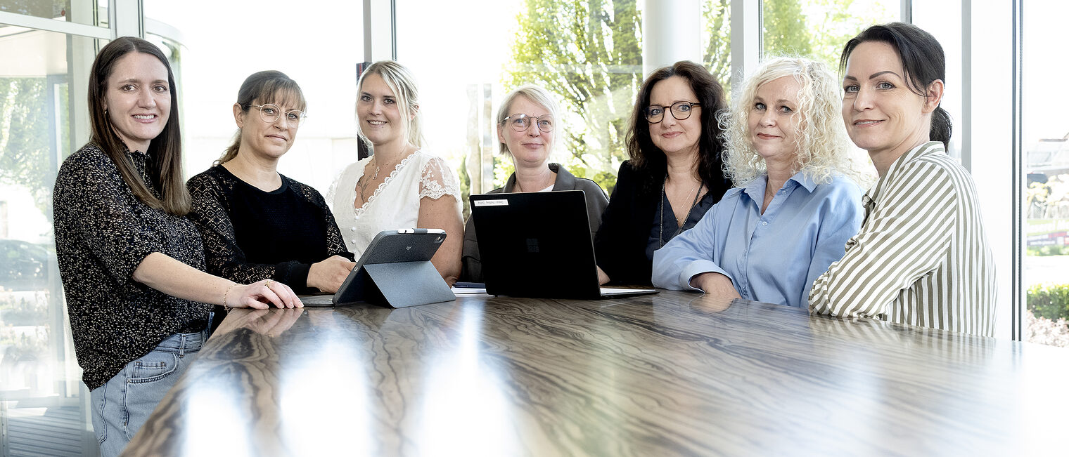 Sieben Frauen nebeneinander an einem Tisch.