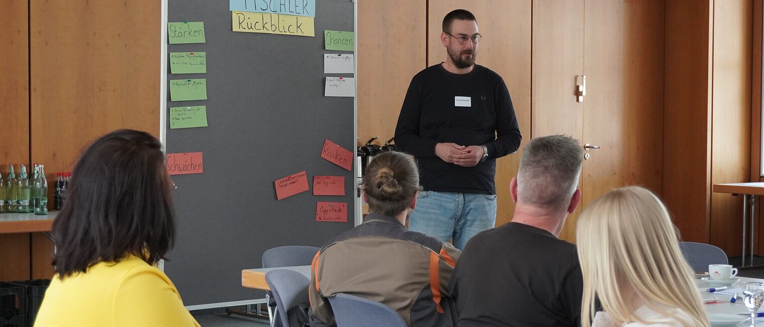 Teilnehmende sitzen auf Stühlen und drehen sch zum Vortragenden um.