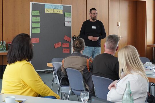 Teilnehmende sitzen auf Stühlen und drehen sch zum Vortragenden um.