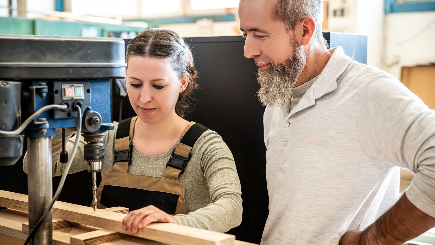 Mädchen wird von Ausbilder an einer Maschine, die Holz bearbeitet, angeleitet.