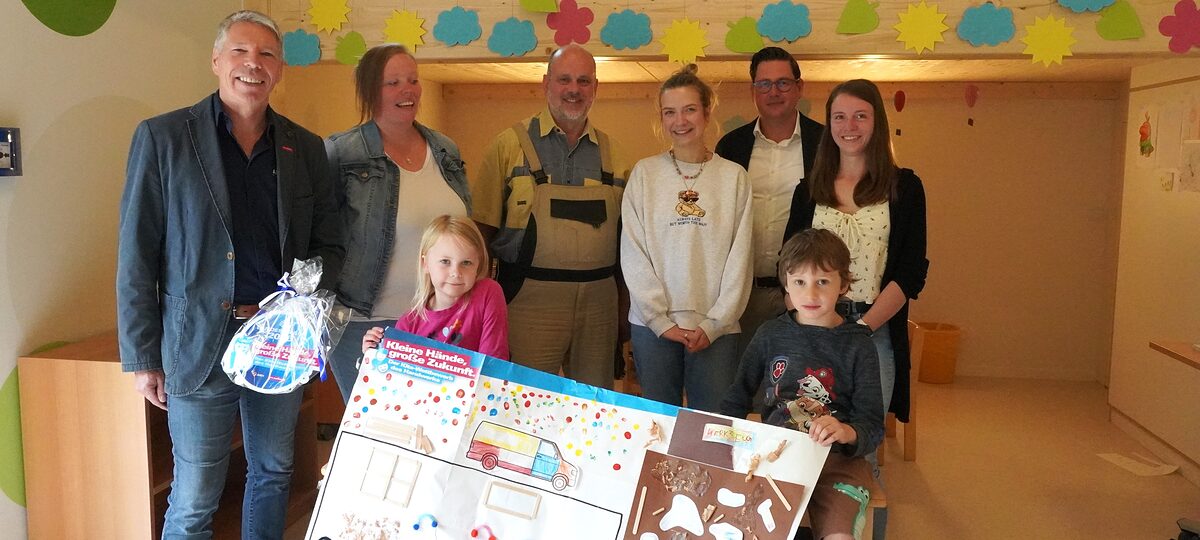Fünf Erwachsene und zwei Kita-Kinder präsentieren das Gewinner-Plakat und die Plakette.