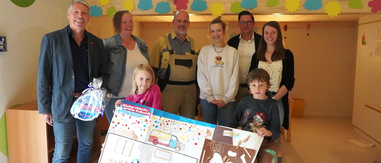 Fünf Erwachsene und zwei Kita-Kinder präsentieren das Gewinner-Plakat und die Plakette.