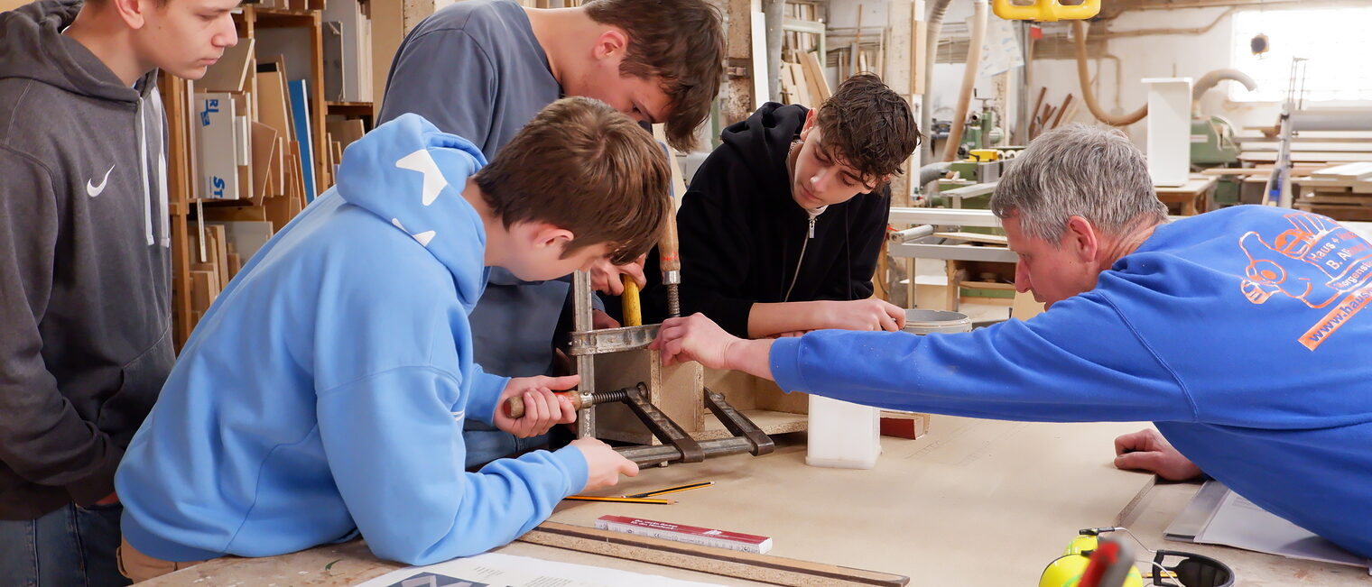 Schülerinnen und Schüler arbeiten in einer Tischlerei an einem Möbelstück.