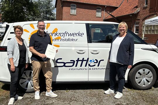 Geschäftsführer Sven Sattler, Ute Sandtvos (Vertreterin des Kultusministeriums) und Bettina Wolf-Moritz (HWK Hannover) bei der Verleihung des Preises für besonders verlässliche Ausbildung vor dem Firmenwagen. 