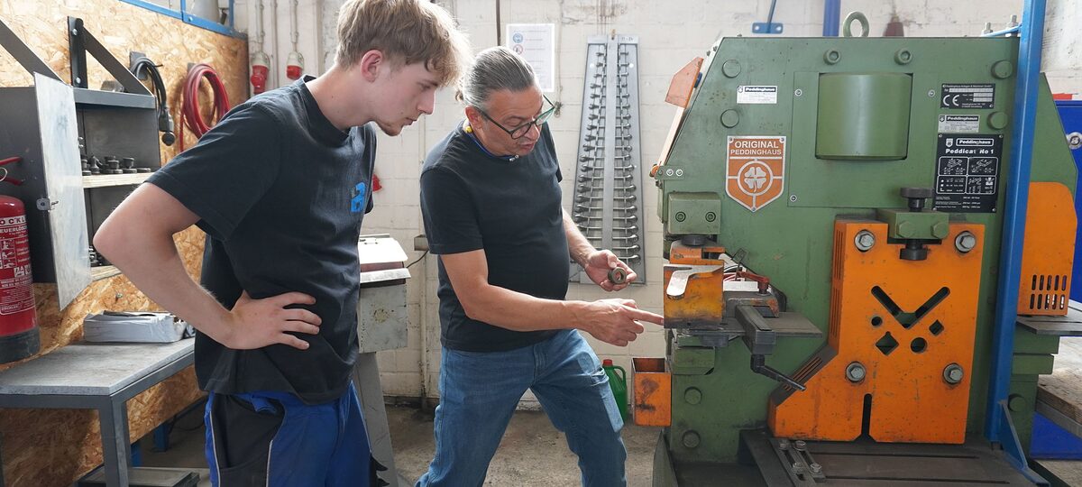 Ausbilder Uwe Wecke und Julius Caspar, Auszubildender zum Metallbauer, in der Ausbildungswerkstatt an einer Maschine.