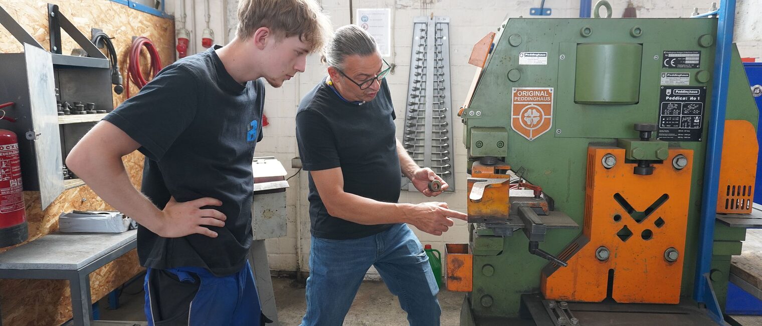 Ausbilder Uwe Wecke und Julius Caspar, Auszubildender zum Metallbauer, in der Ausbildungswerkstatt an einer Maschine.