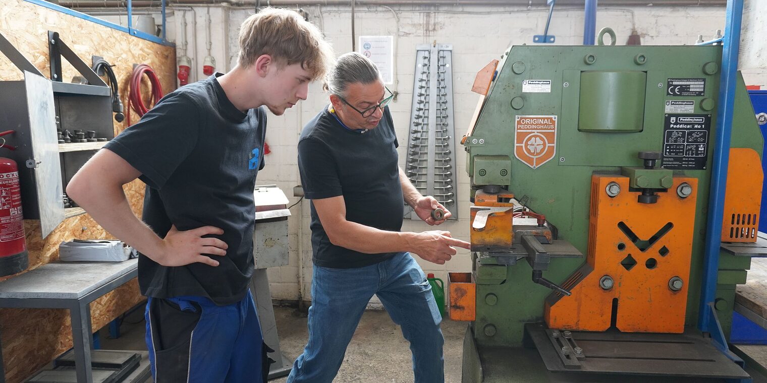 Ausbilder Uwe Wecke und Julius Caspar, Auszubildender zum Metallbauer, in der Ausbildungswerkstatt an einer Maschine.