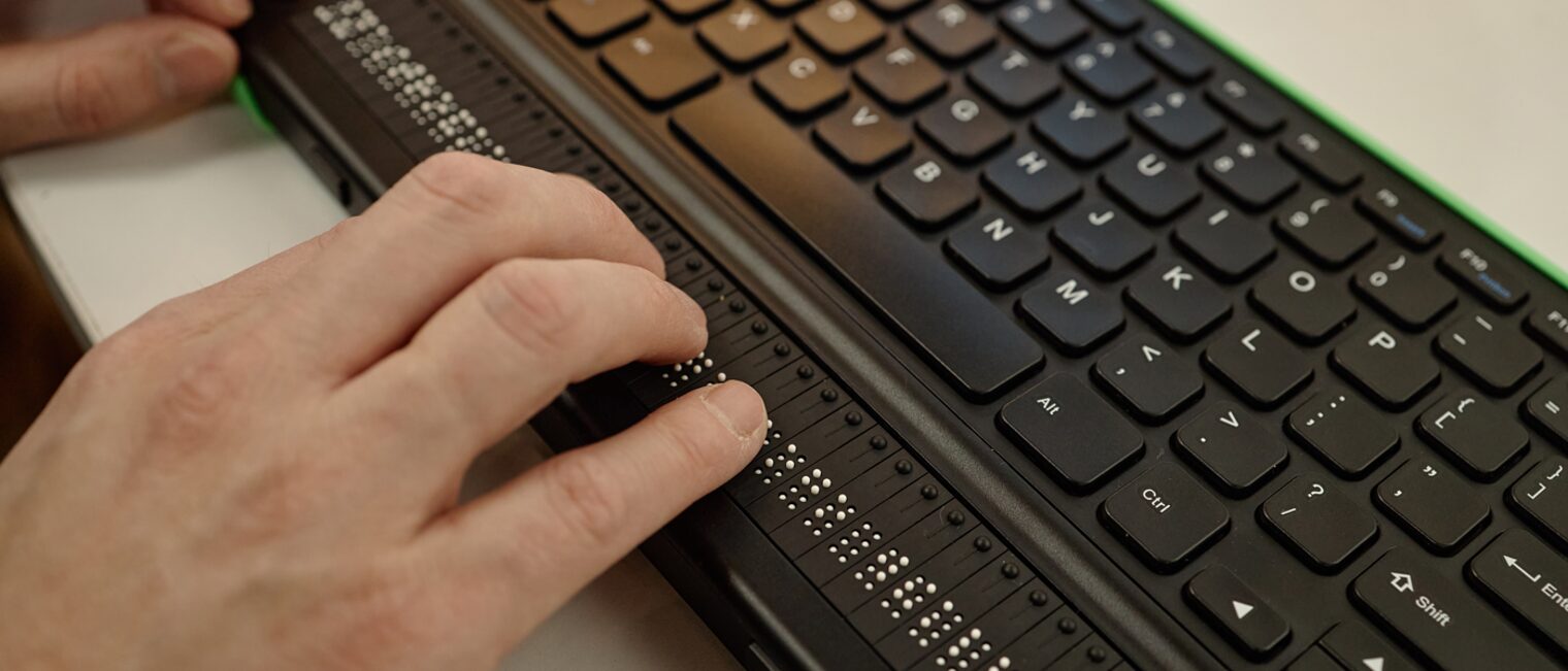 Person, die Braille-Schrift auf einer Tastatur liest.