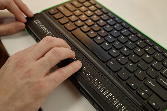 Person, die Braille-Schrift auf einer Tastatur liest.