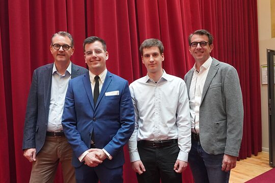 Die vier Männer stehen vor einem roten Vorhang.